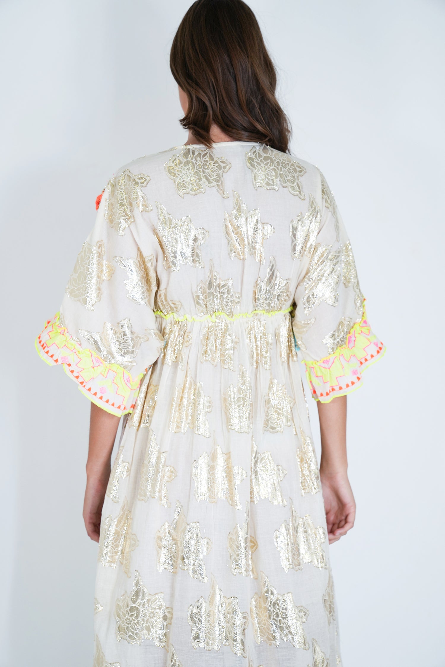 Woman wearing a white embroidered dress with colorful trim on a plain background