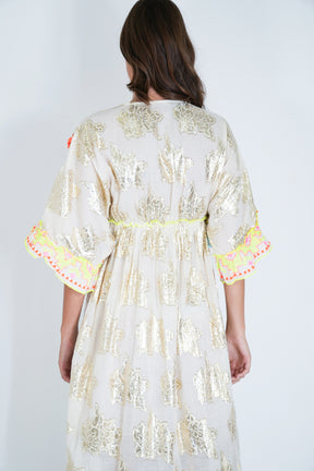 Woman wearing a white embroidered dress with colorful trim on a plain background