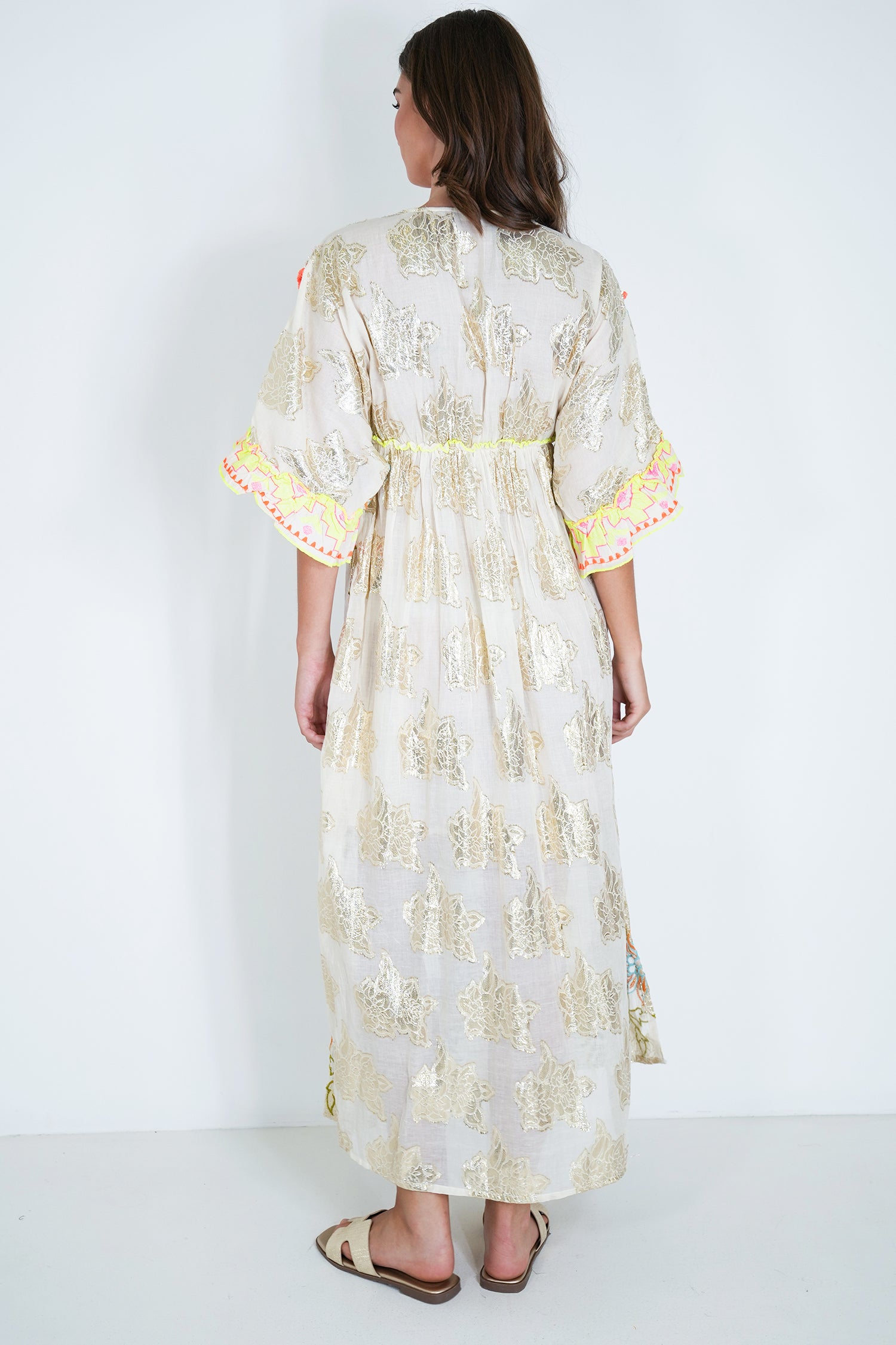 Woman wearing a long, light-colored dress with floral patterns on a white background