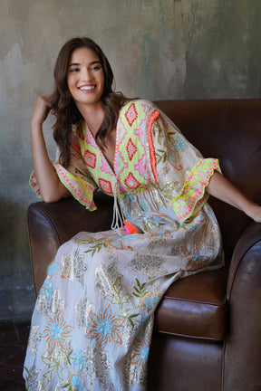 Woman sitting on a brown leather couch wearing a colorful embroidered dress.