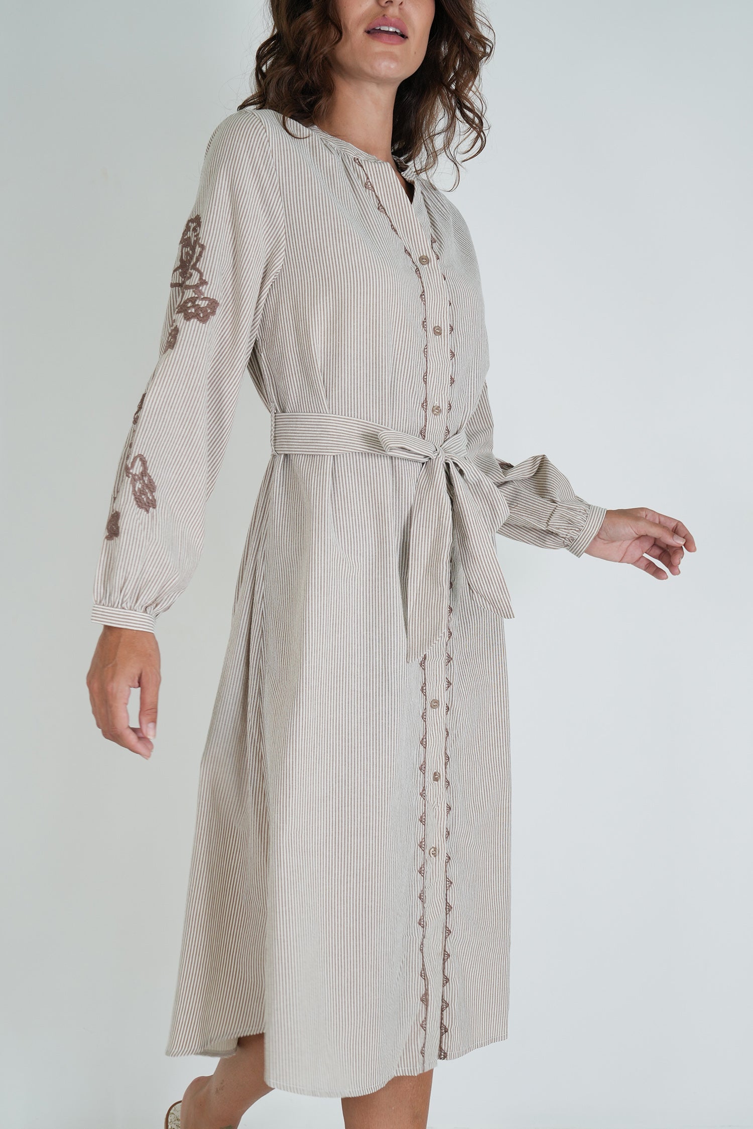 Woman wearing a beige dress with floral embroidery on a white background