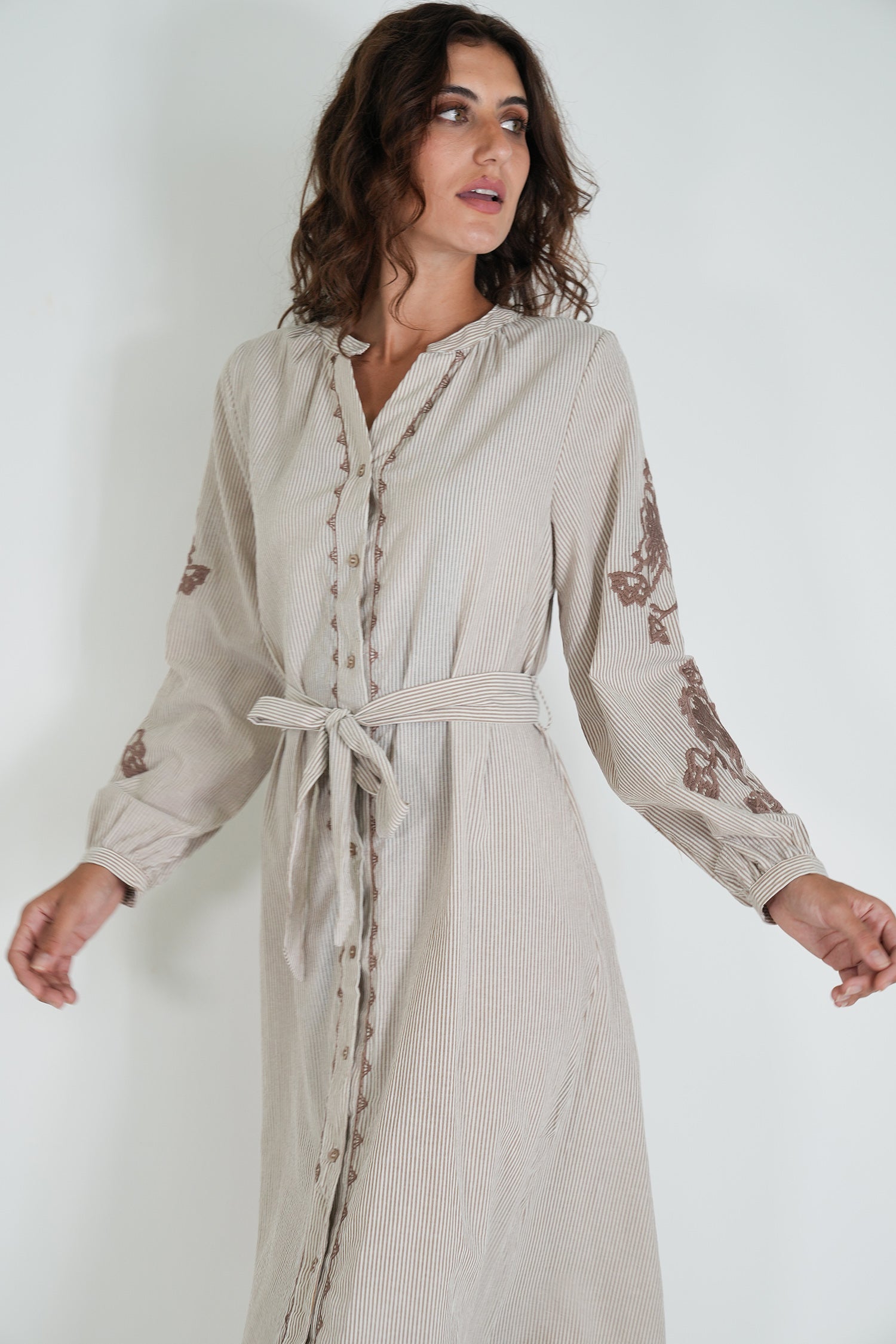 Woman wearing a beige dress with floral embroidery on a white background