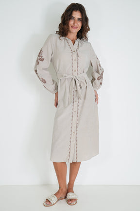 Woman wearing a beige dress with floral embroidery on a white background