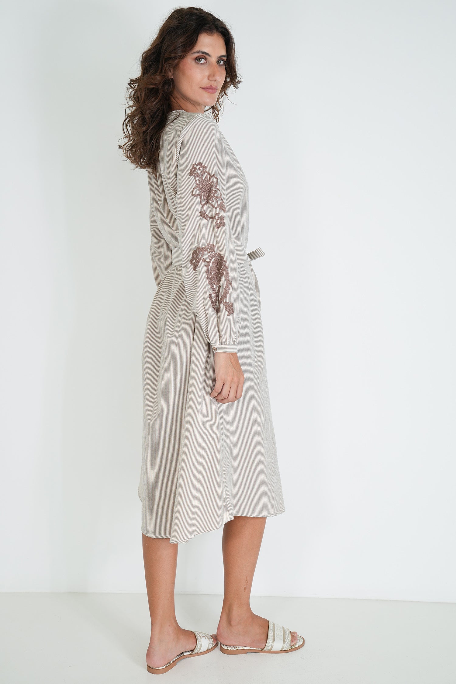 Woman wearing a beige dress with floral embroidery on a white background