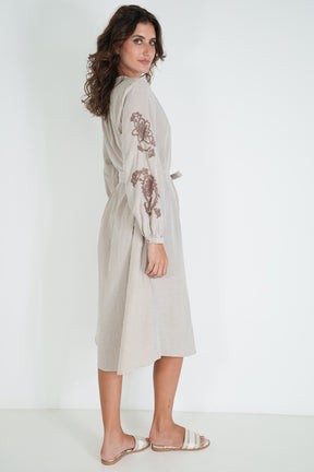 Woman wearing a beige dress with floral embroidery on a white background