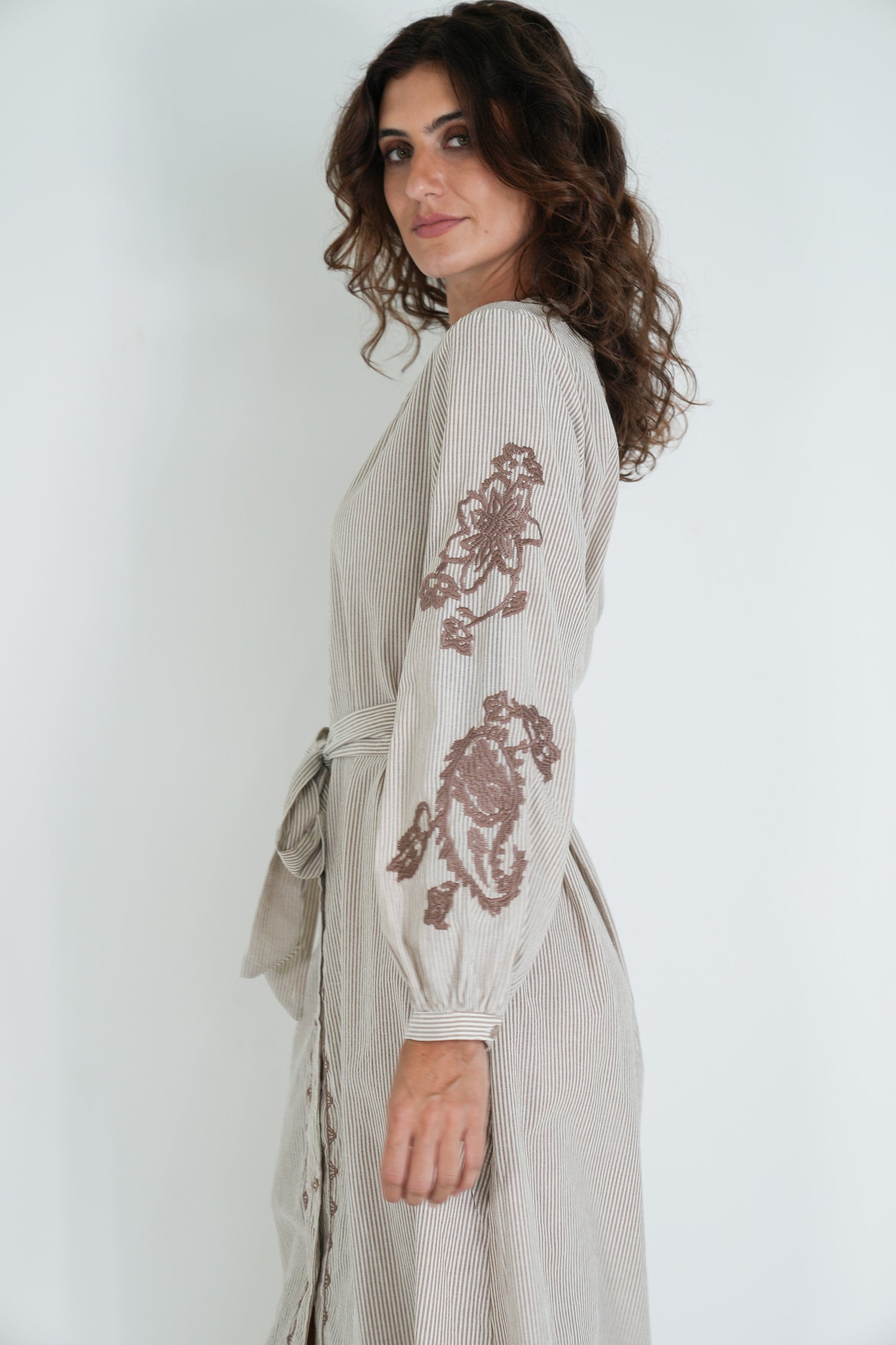 Woman wearing a light-colored dress with floral embroidery on a white background