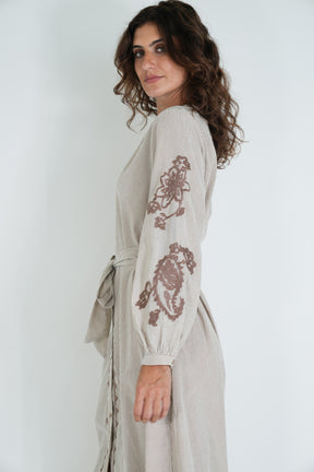Woman wearing a light-colored dress with floral embroidery on a white background