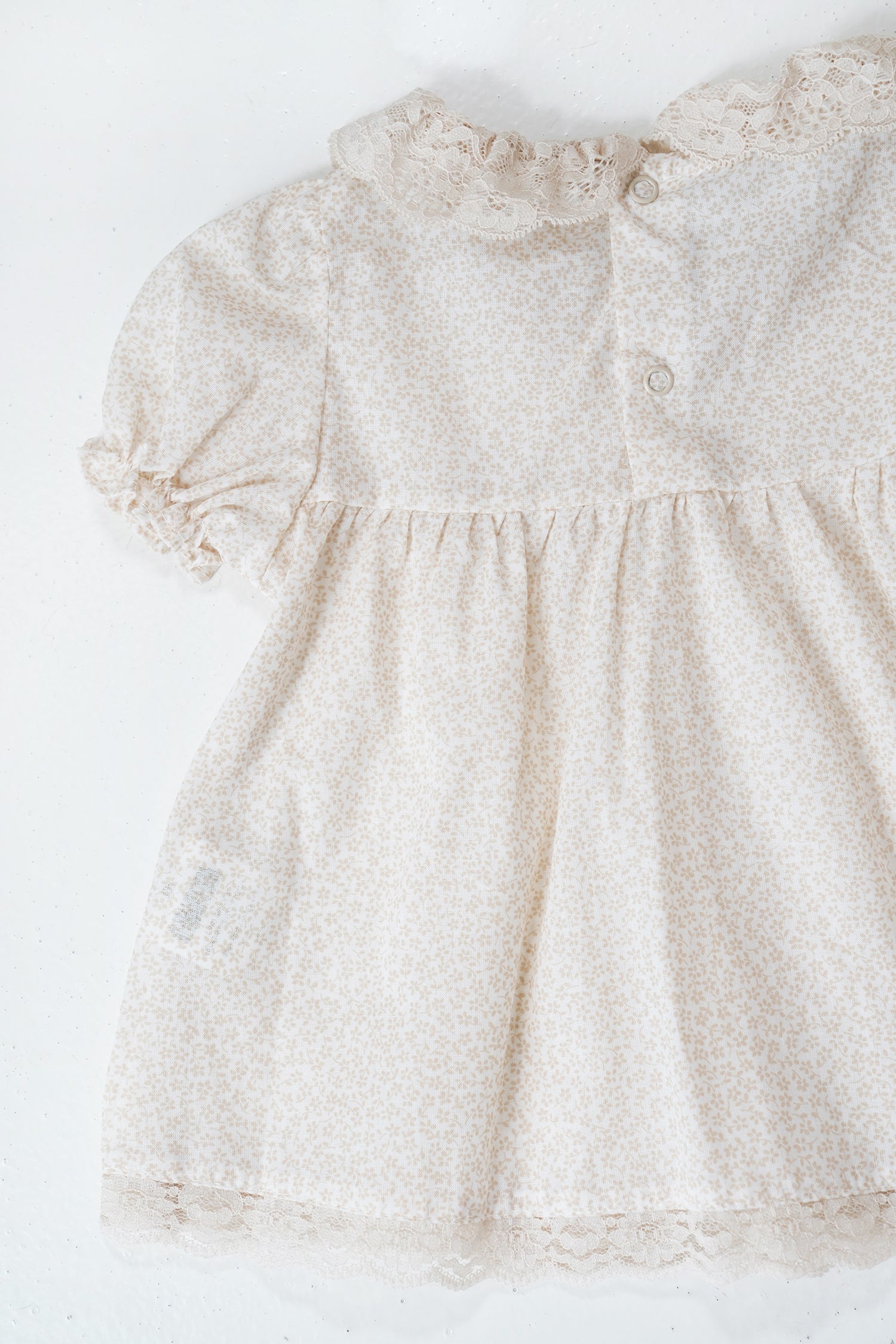 Beige baby dress with lace details on a white background