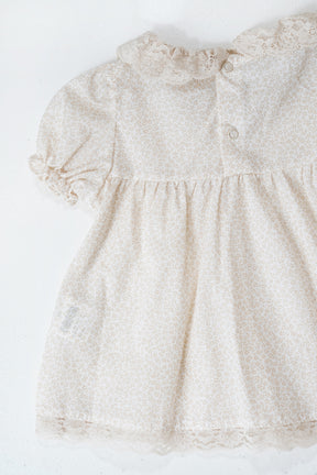 Beige baby dress with lace details on a white background