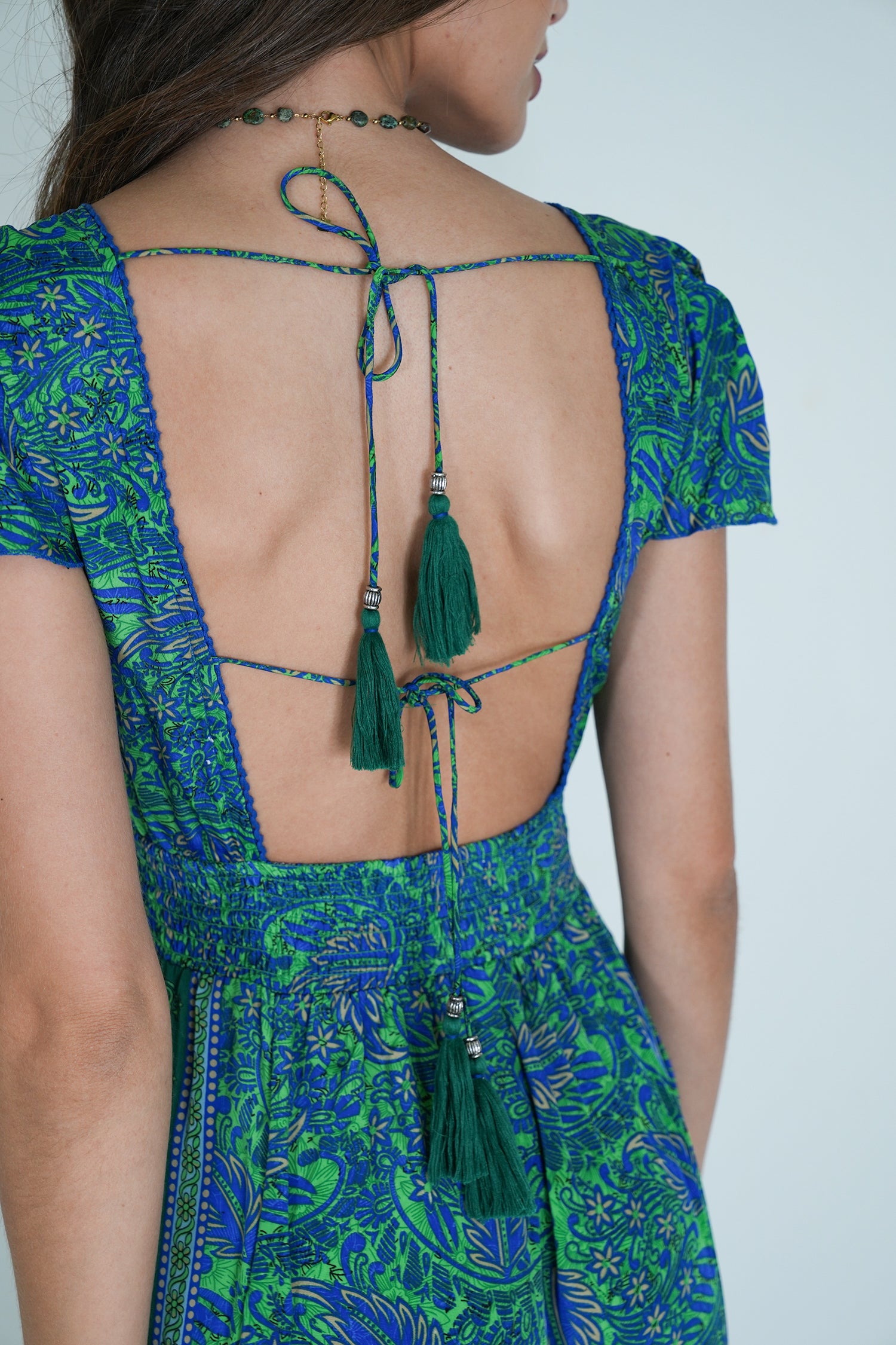 Green and blue patterned dress with open back and tassels on a plain background