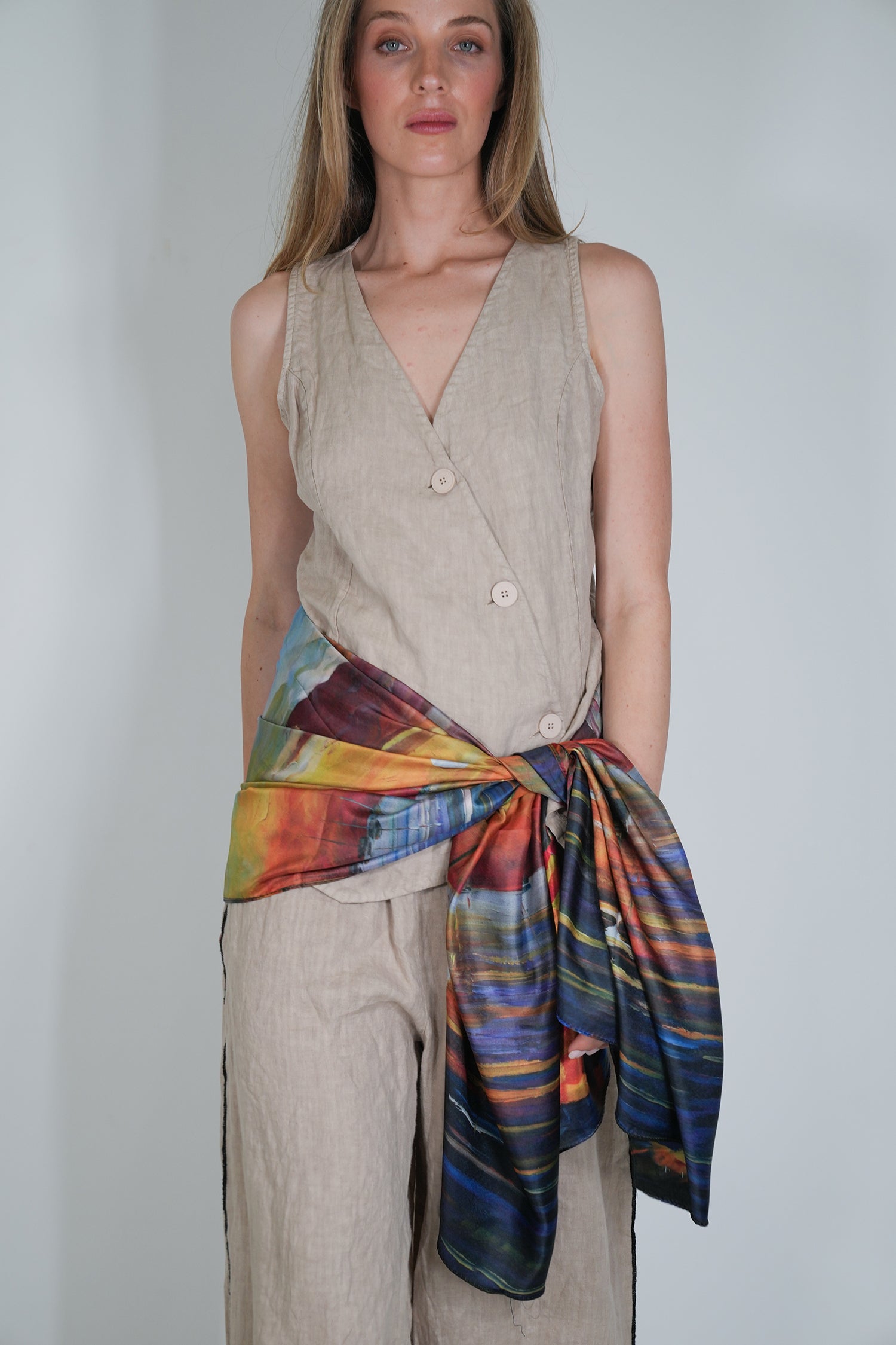 Woman wearing a beige sleeveless top and colourful scarf against a plain background