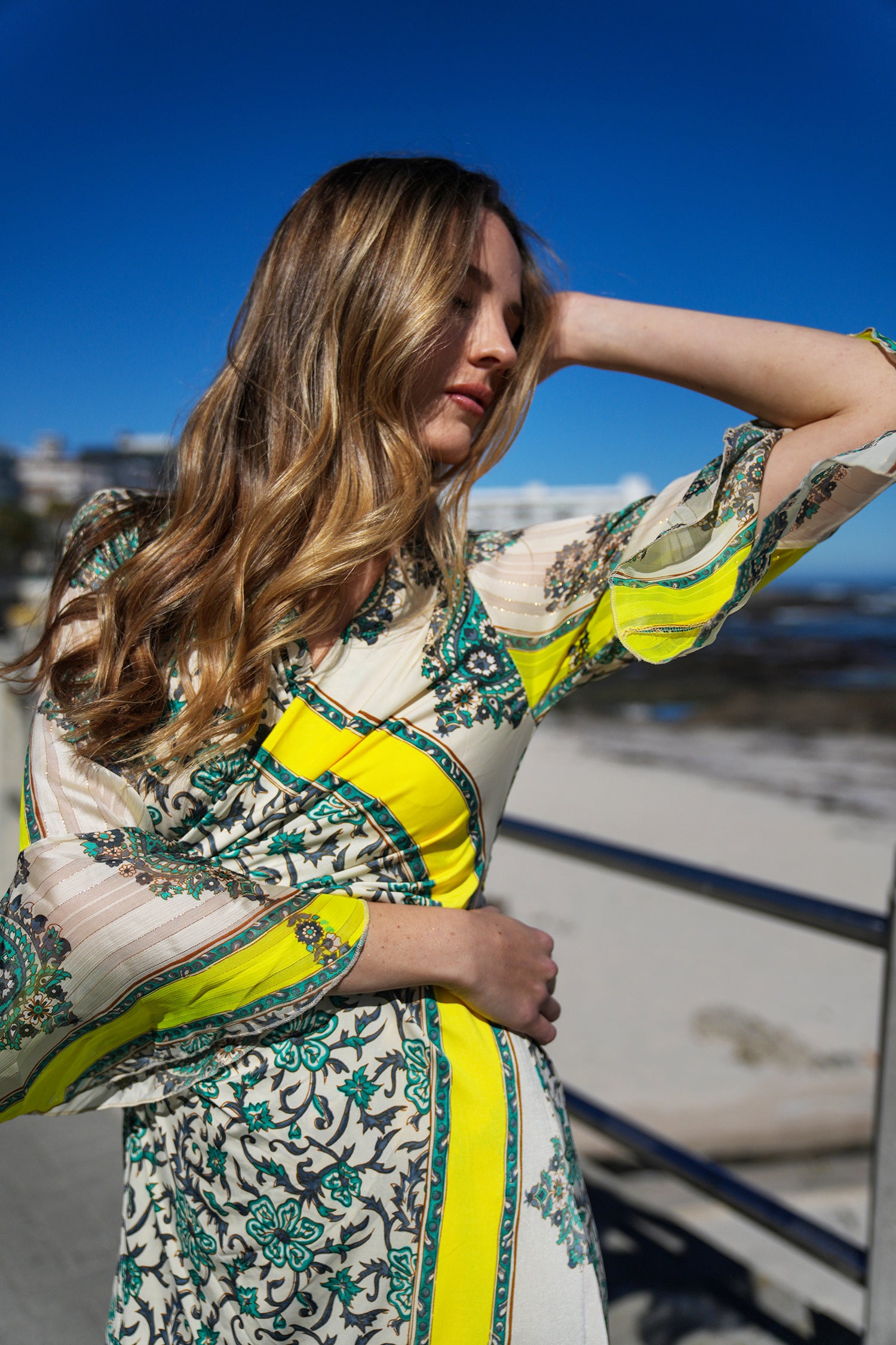 Woman wearing a patterned dress with yellow accents against a blue sky.