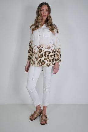Woman wearing a white blouse with a leopard print pattern and white pants on a plain background