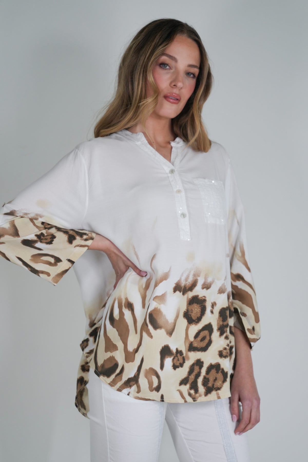 Woman wearing a white blouse with leopard print sleeves against a plain background