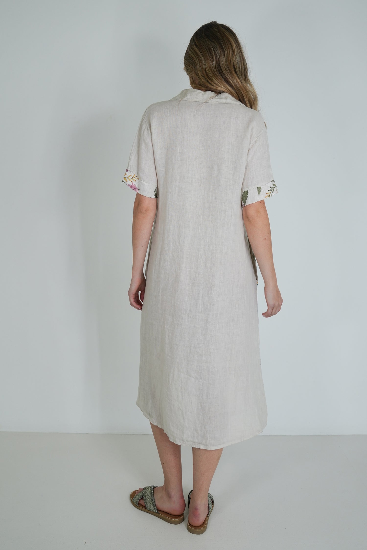 Woman wearing a light-colored dress with rolled-up sleeves on a plain background