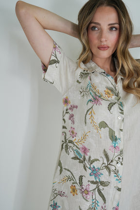 Woman wearing a floral embroidered shirt against a plain background