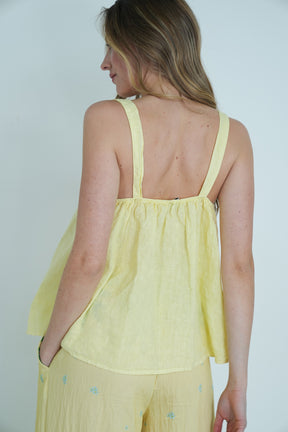 Woman wearing a yellow sleeveless top and pants against a plain background