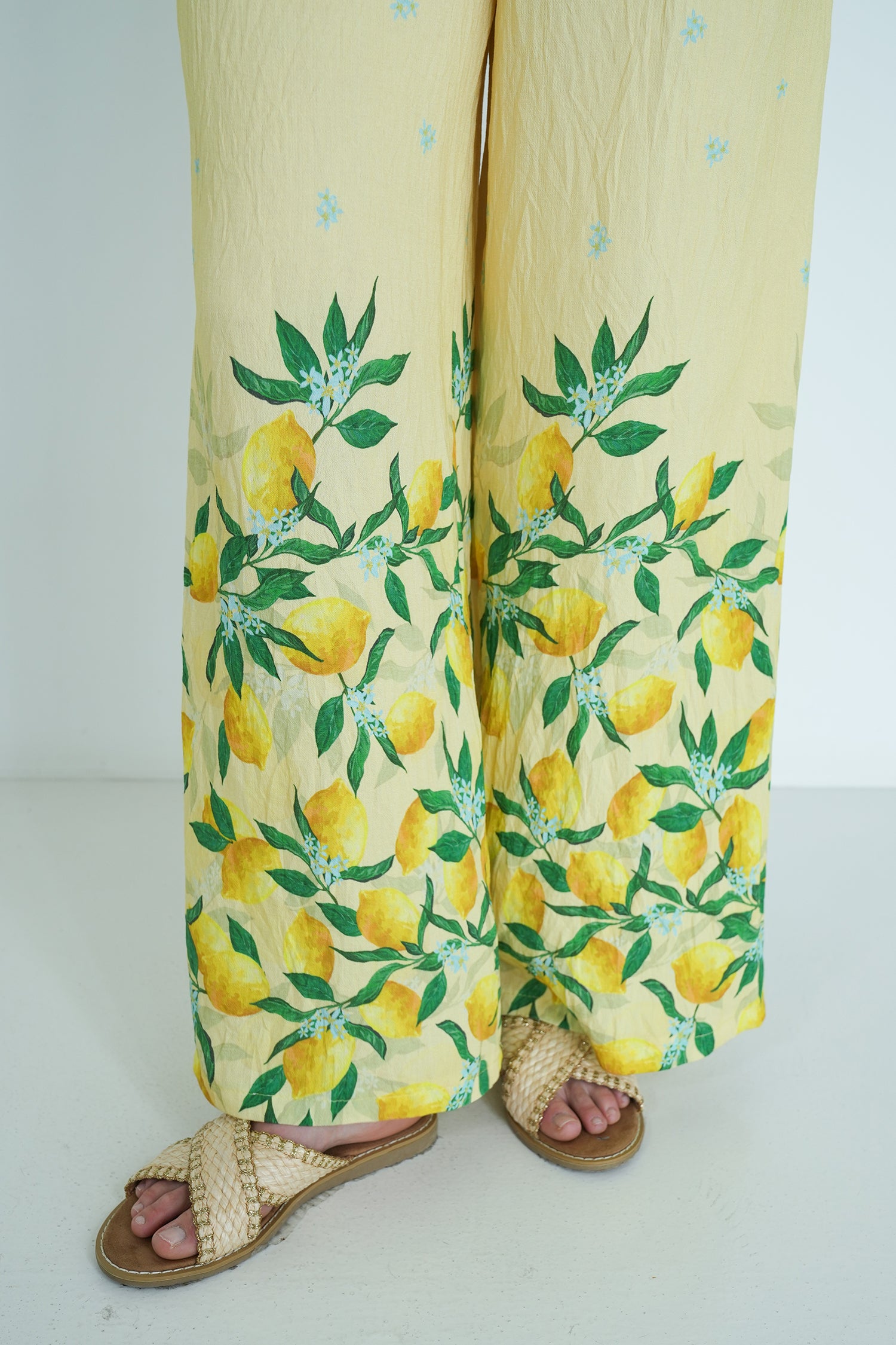Yellow pants with lemon and leaf pattern worn by a person on a white background