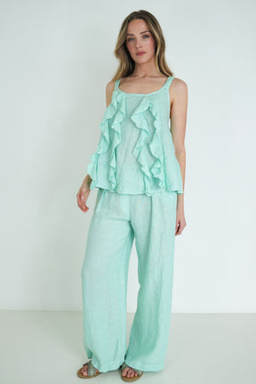 Woman wearing a mint green ruffled top and wide-leg pants on a white background