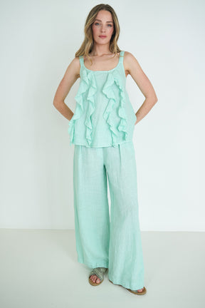 Woman wearing a mint green ruffled top and wide-leg pants on a white background