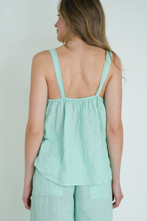 Woman wearing a light green sleeveless top and pants against a plain background