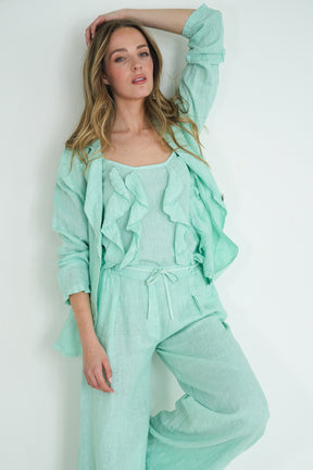 Woman wearing a mint green outfit with ruffled details against a white background