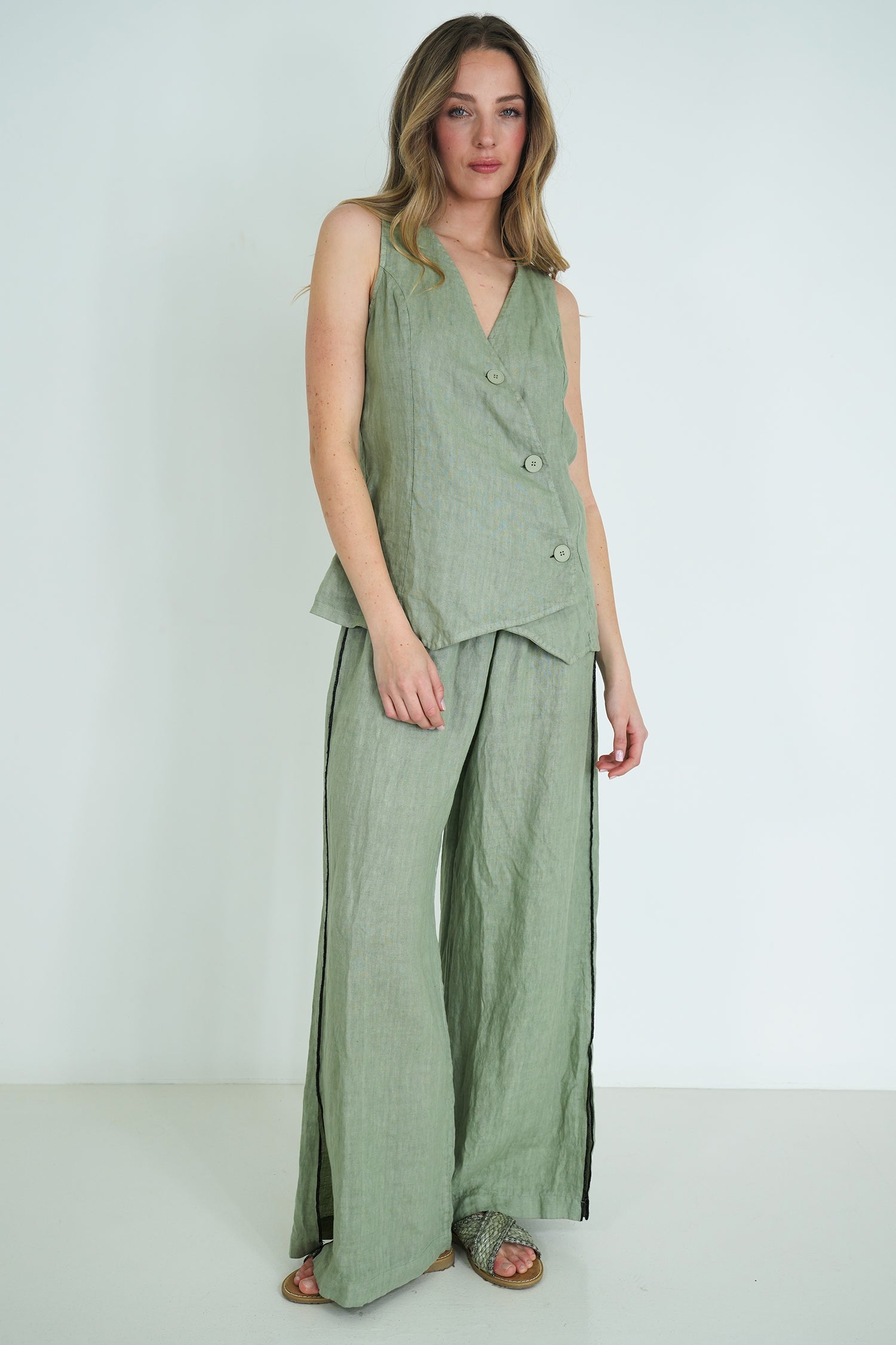Woman wearing a green sleeveless top and wide-leg pants against a white background