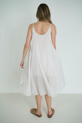 Woman wearing a white dress with thin straps on a plain background