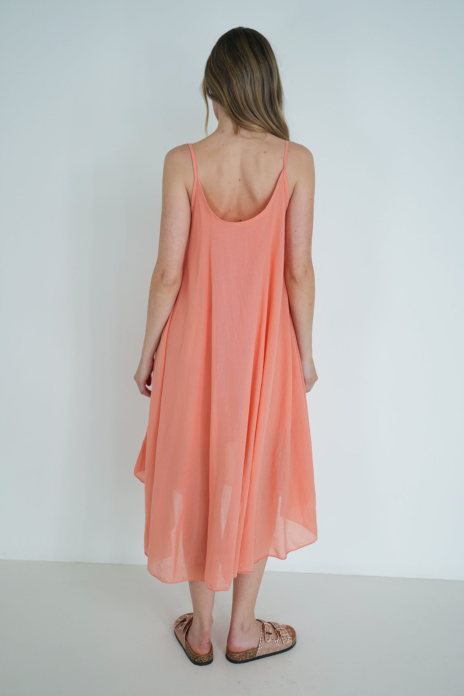 Woman wearing a peach-colored dress with thin straps against a white background