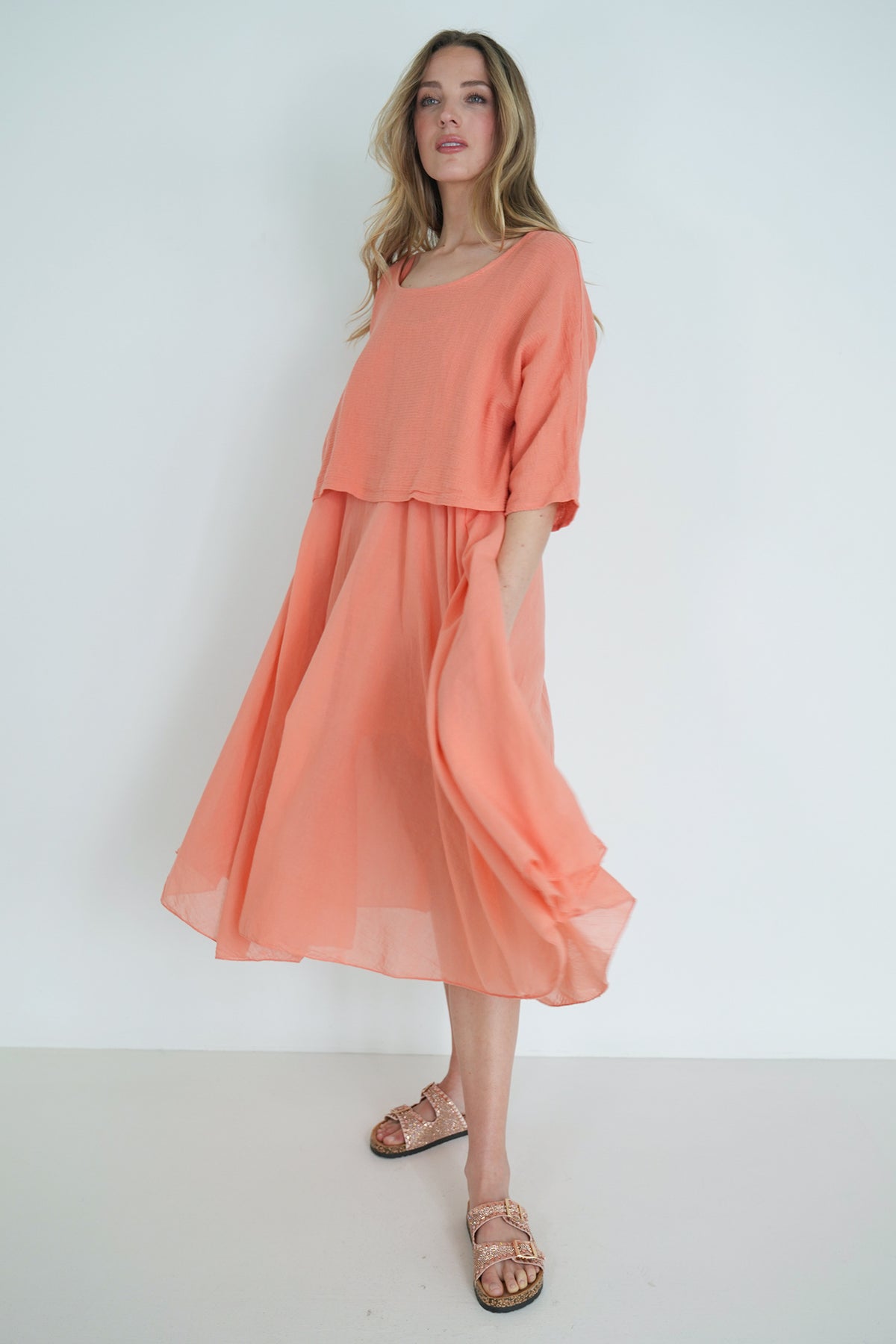 Model walking in coral flowy midi dress with soft pleats and relaxed fit, styled for an effortless elegant look."