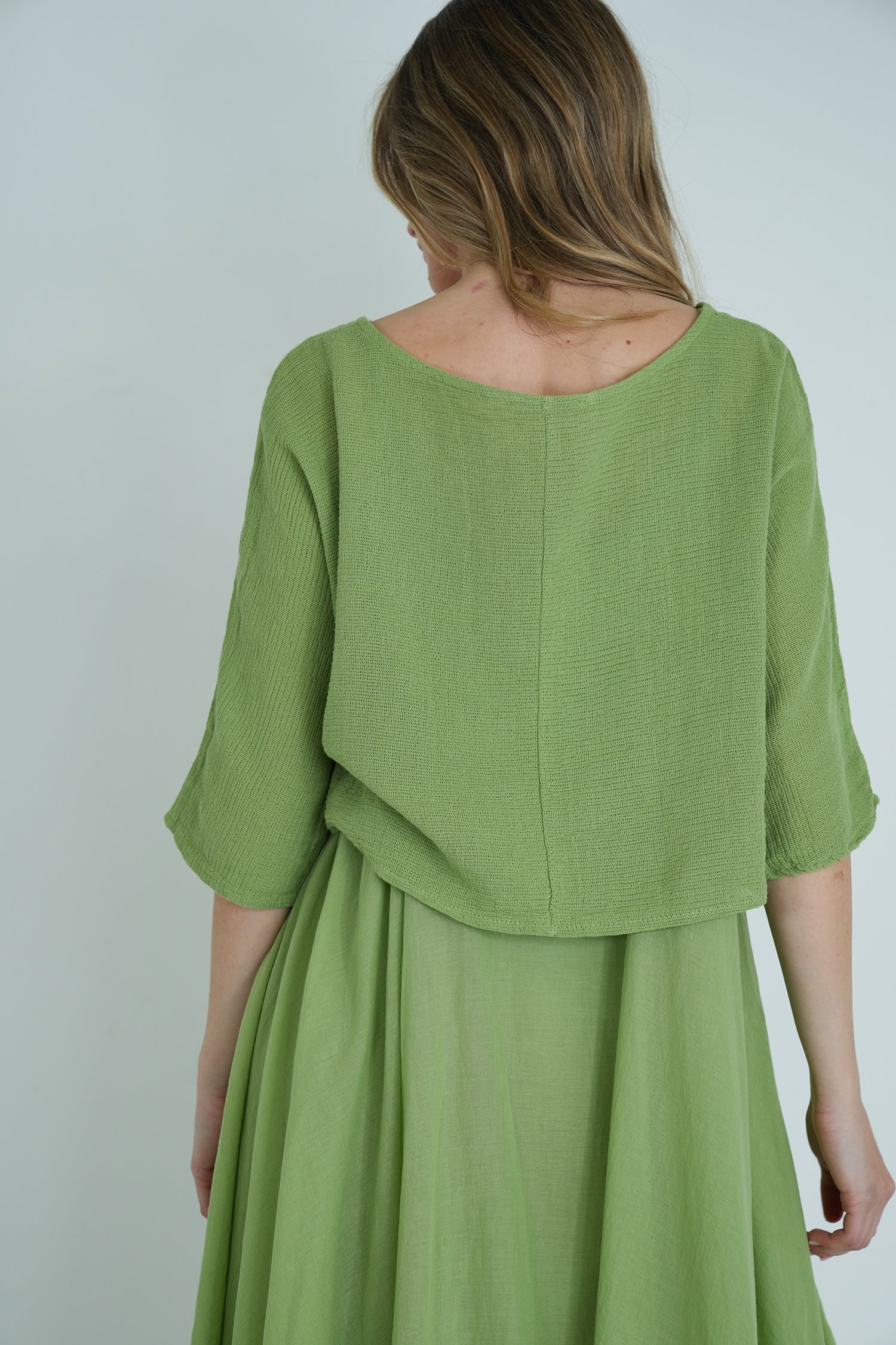 Back view of model wearing a light green textured knit top paired with a flowy green midi skirt, showing relaxed fit and drape.