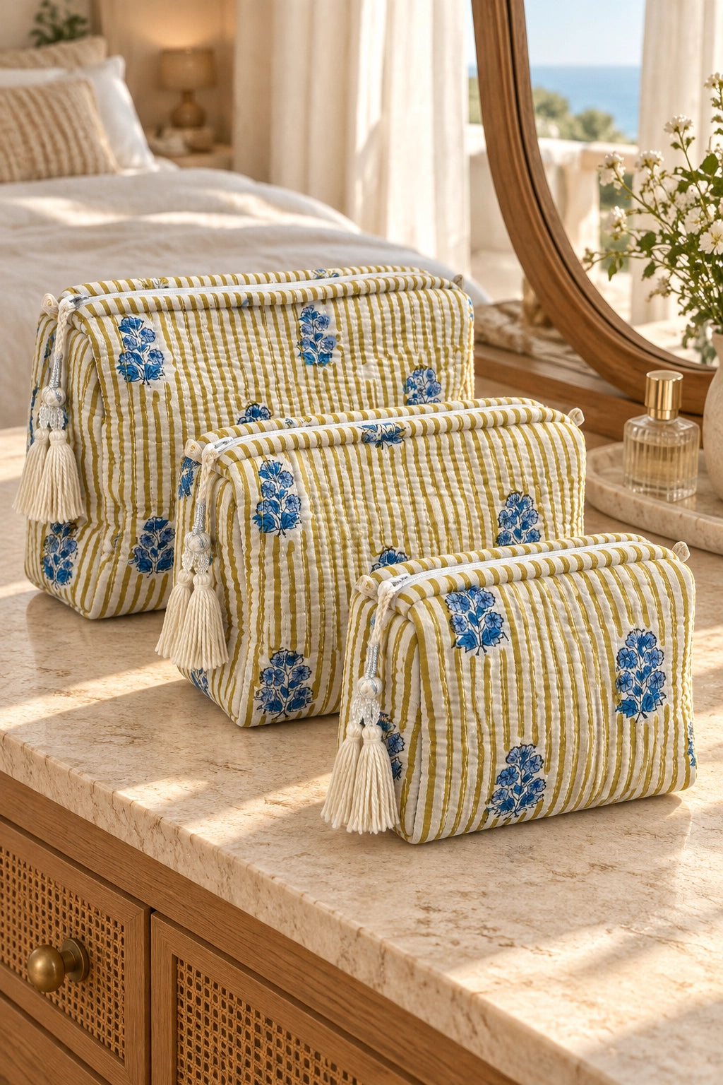 Three small zippered cosmetic pouches with tassel pulls in a yellow-and-white gingham pattern with blue floral motifs, arranged on a marble bathroom counter.