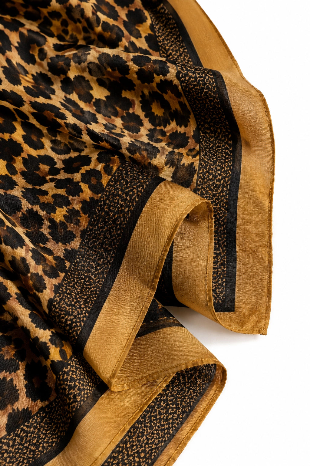 A close-up of a leopard-print scarf with a wide tan border and black patterned trim, laid out on a white background.