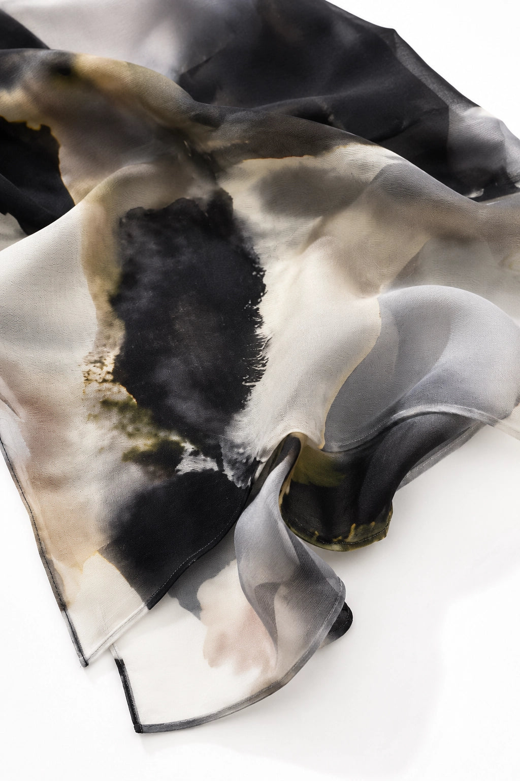 A lightweight sheer scarf with an abstract watercolor design in black, gray, beige, and white, draped elegantly on a white surface.