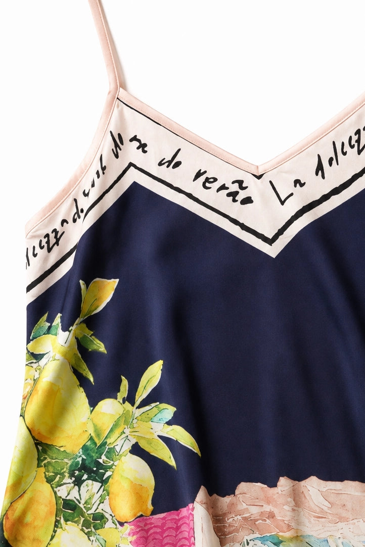 Close-up of a camisole top with a navy blue base, featuring a yellow lemon and green leaf print on the lower left, a beige script trim with black lettering across the neckline, and a pink textured band near the bottom.