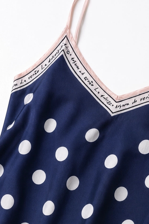 Close-up of a navy blue camisole or tank top with large white polka dots and thin light pink straps, shown against a plain white background.