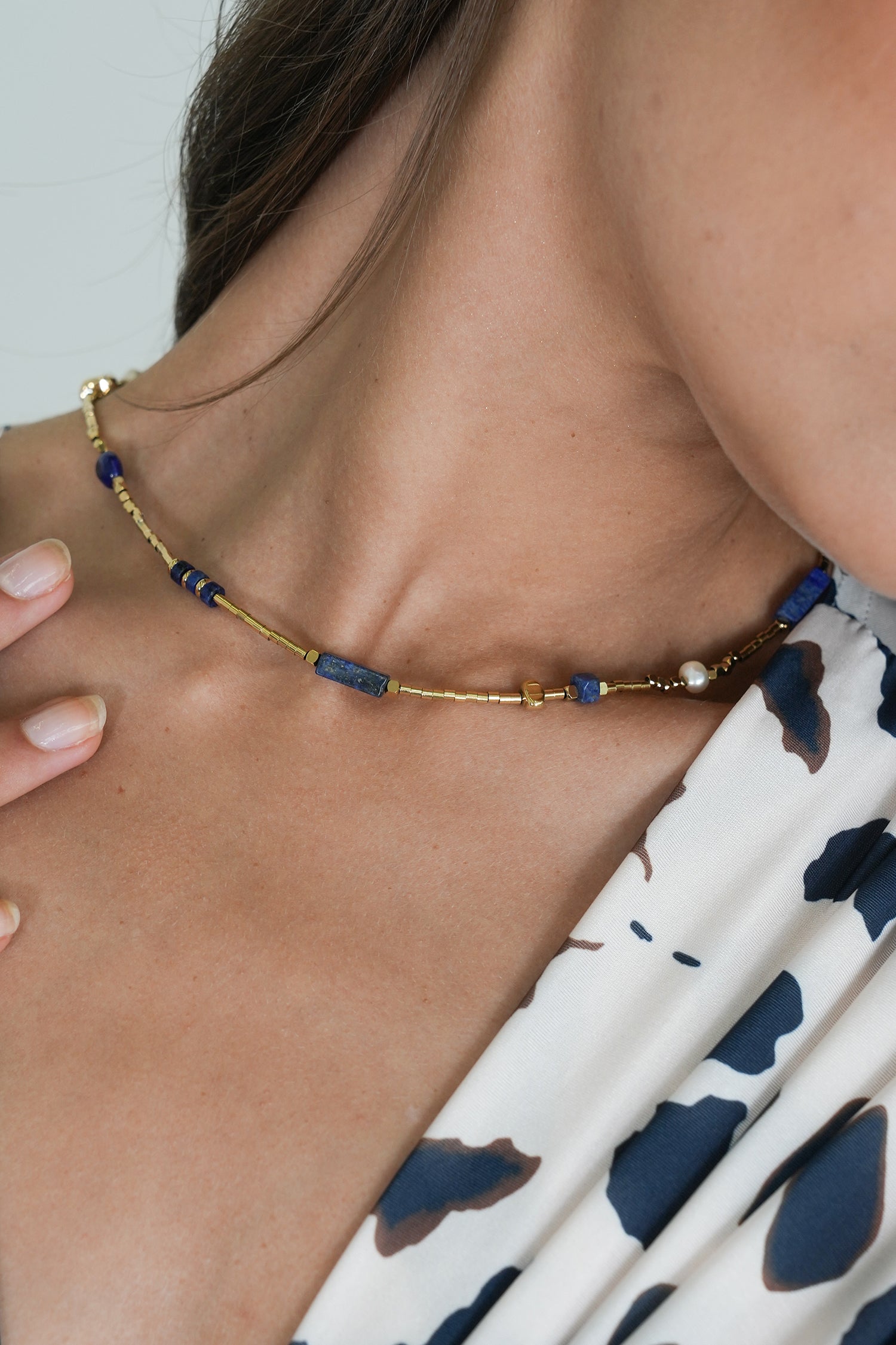 Necklace with blue beads and gold accents worn by a person with a patterned garment.