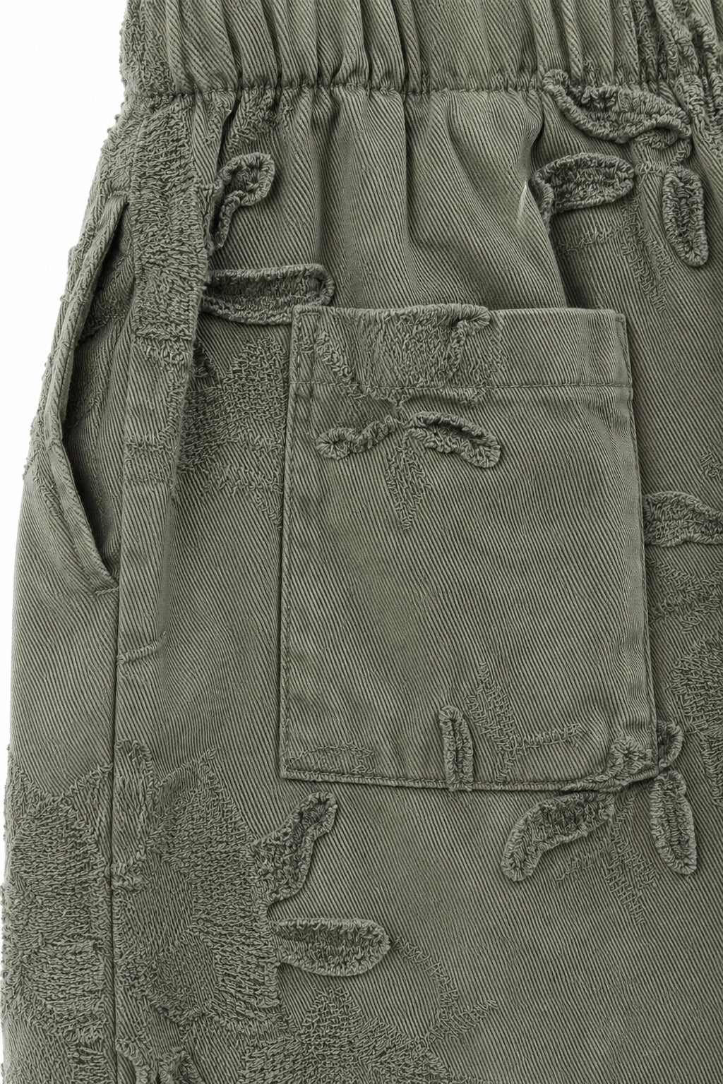 Close-up of olive green pants featuring a textured, raised leaf pattern and a front patch pocket.
