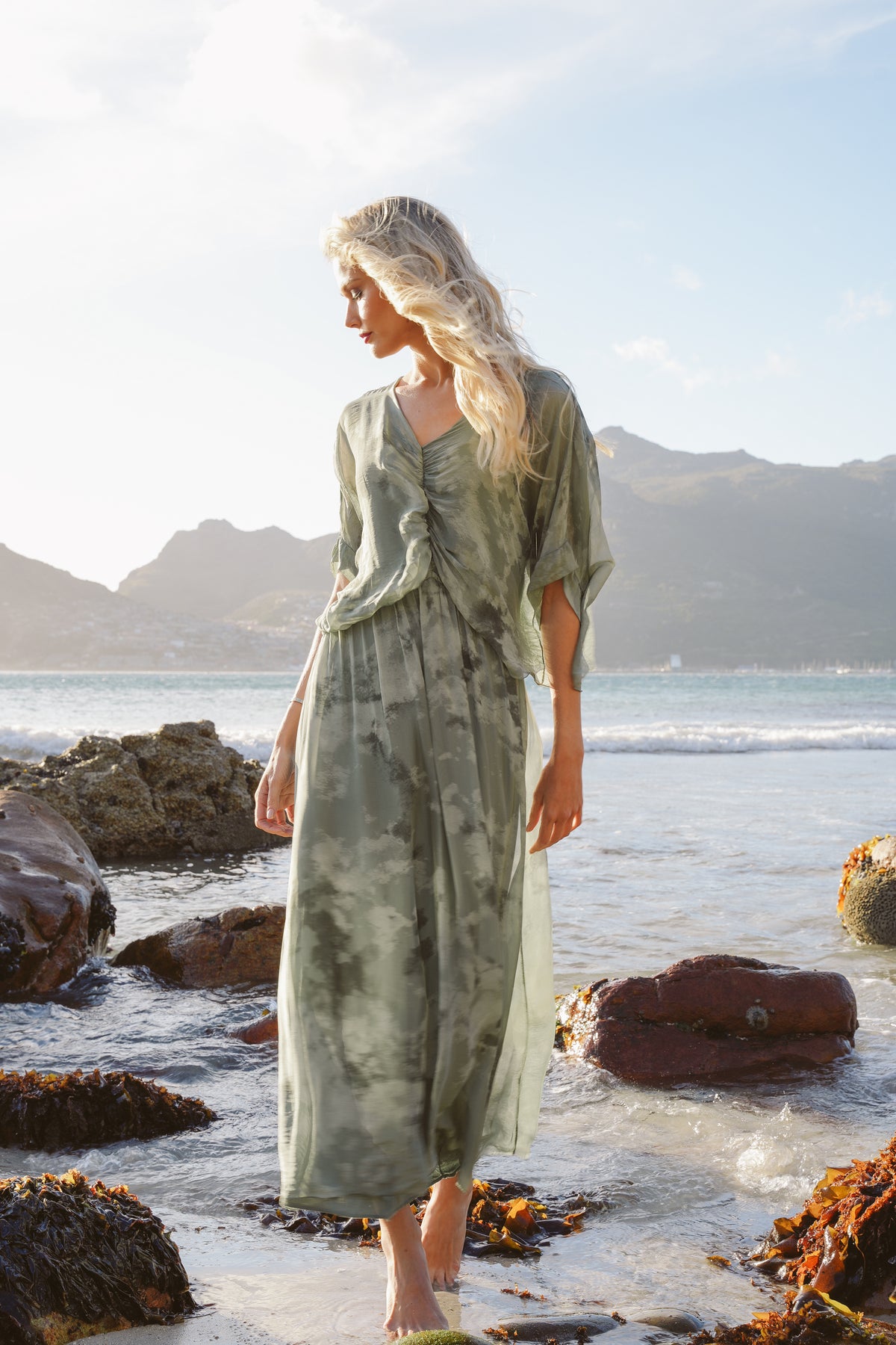 Woman in a green dress standing on a beach with mountains in the background