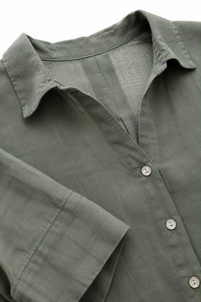 Close-up of a muted sage green linen button-up shirt, showing the textured fabric, collar, and buttons.