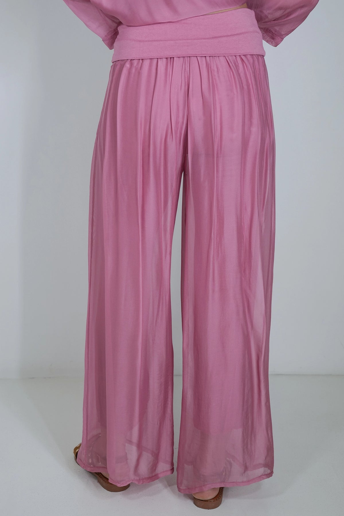 A person wearing loose, wide-leg pink pants with a matching waistband, shown from the back against a plain light gray studio background.
