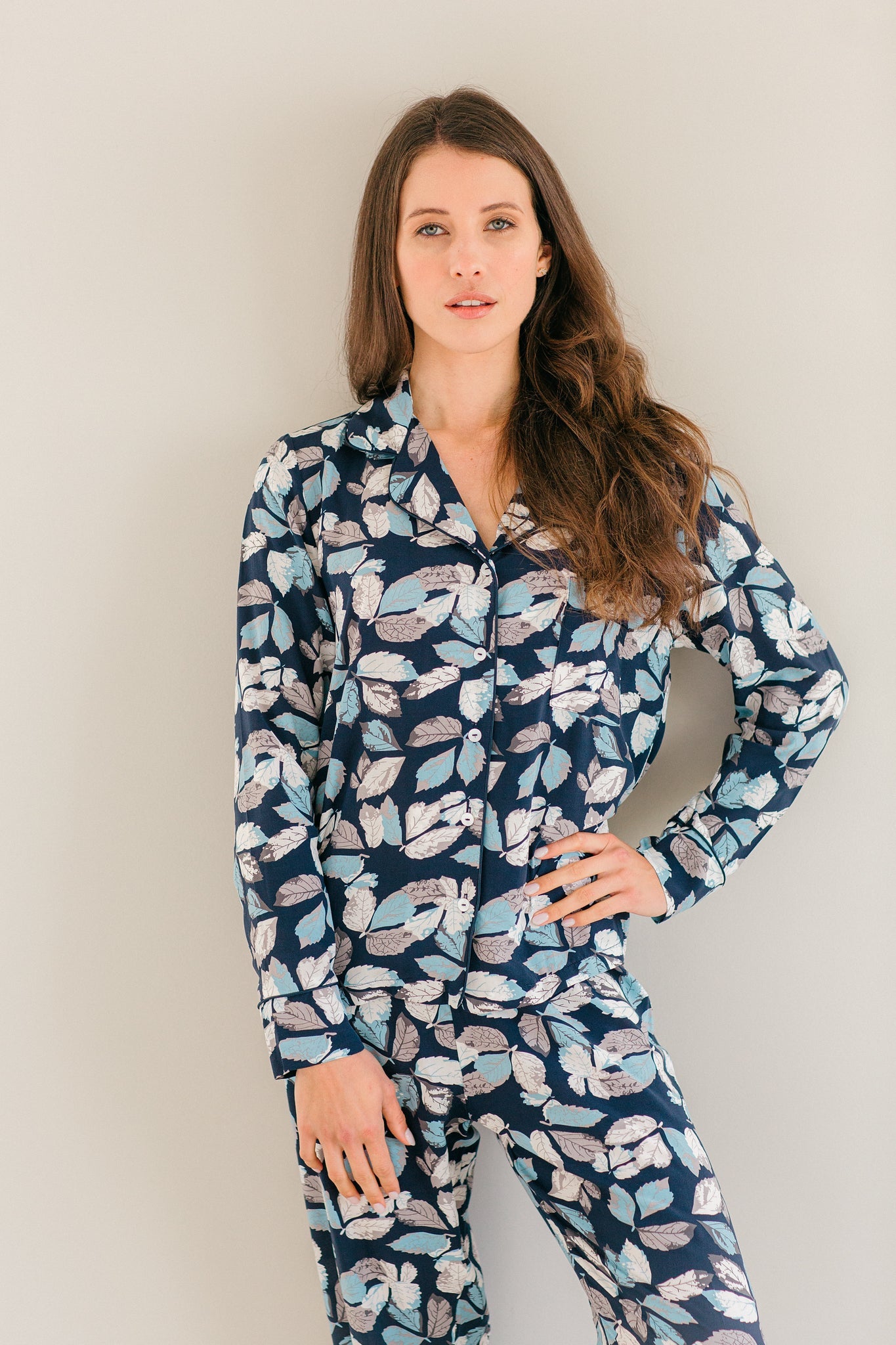 A woman modeling a matching long-sleeve pajama set with a navy blue base and a light blue, white, and pink floral pattern, set against a plain light gray background.