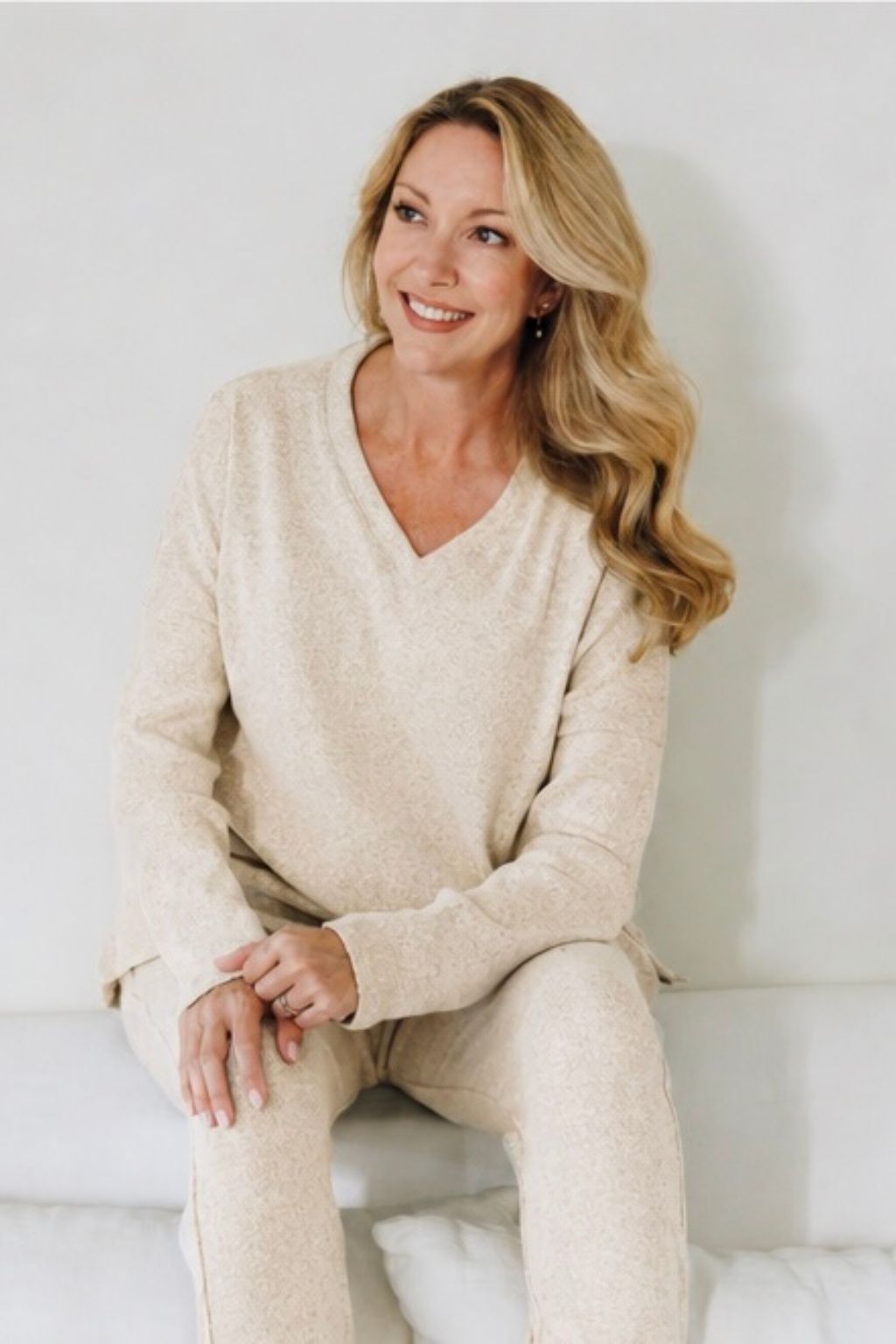 Woman wearing a beige sweater and pants sitting on a white couch.