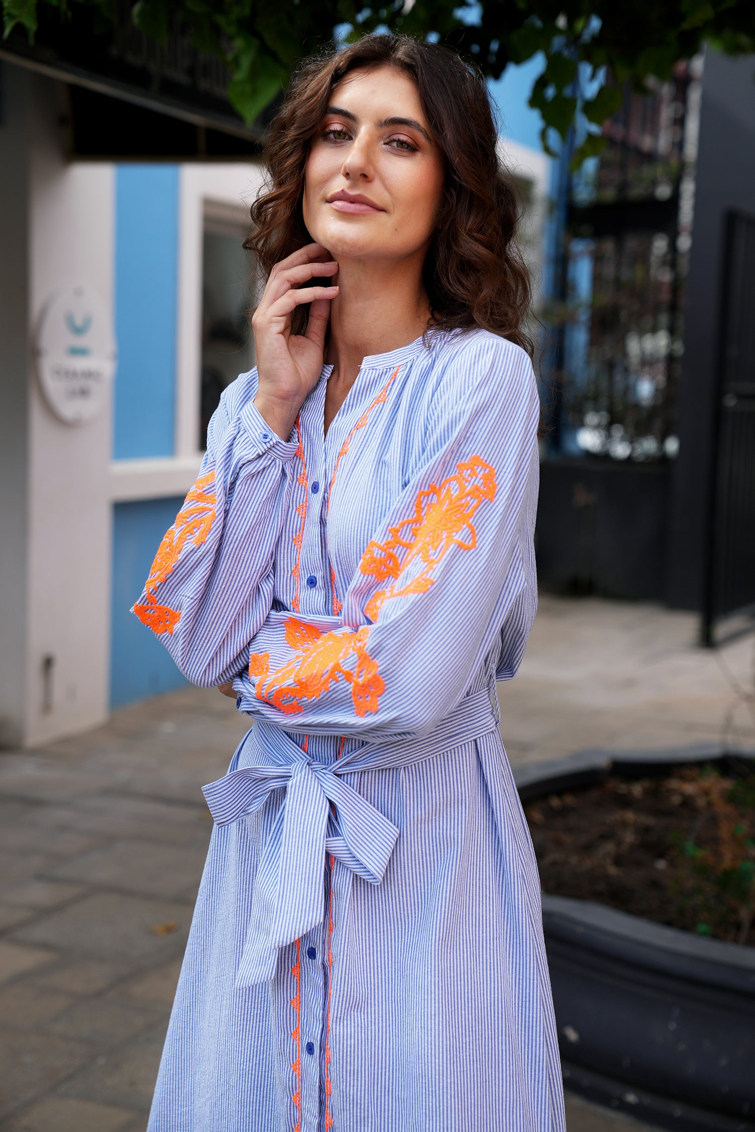 Woman wearing a light blue dress with orange floral embroidery outdoors.