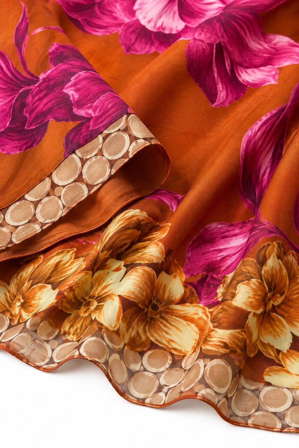 A close-up of a draped orange-brown scarf featuring a vibrant magenta floral pattern and a scalloped border with tan and brown floral motifs.