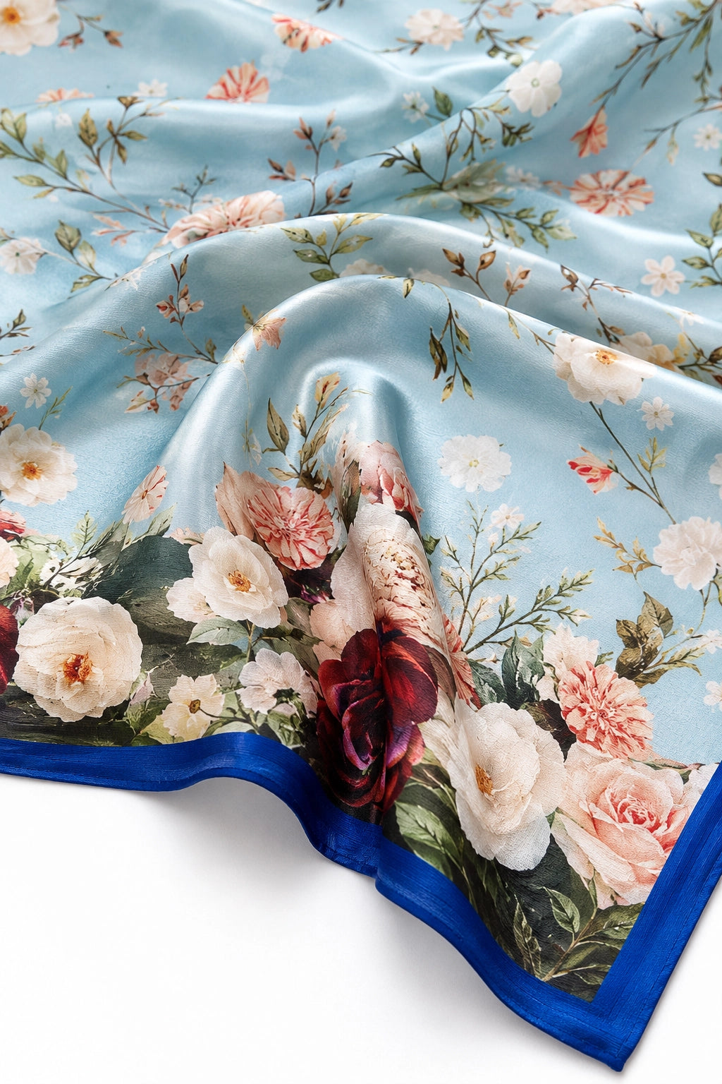A square silk scarf with a light blue background, featuring a dense floral print with pink, white, and dark red roses, green leaves, and a solid royal blue border.