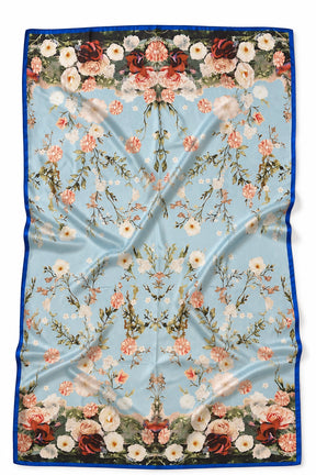 A square silk scarf featuring a light blue background with a symmetrical floral pattern and a dark blue border, laid flat with soft folds.