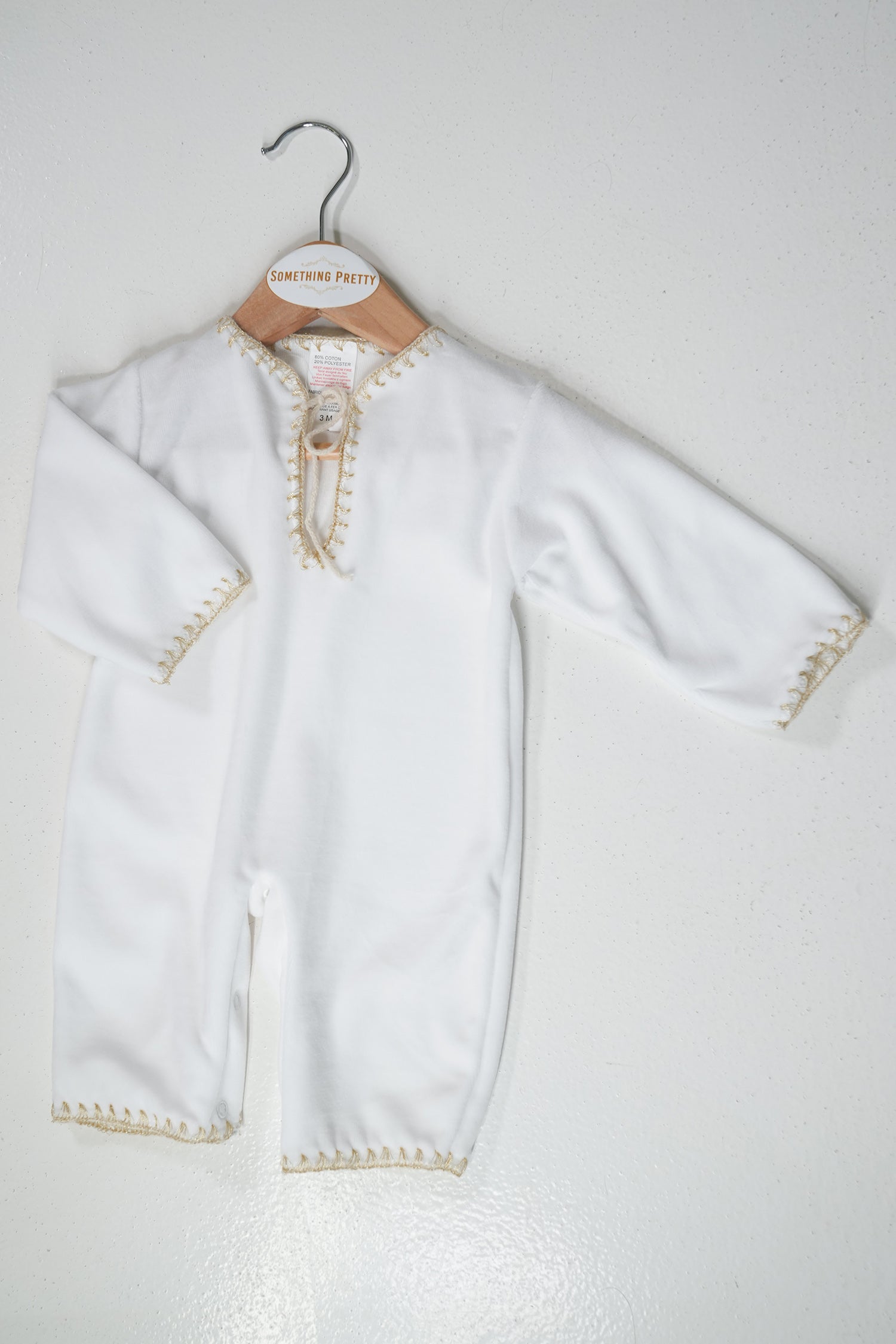 White baby outfit with gold trim on a hanger against a white background
