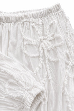 Close-up of white textured fabric with raised embroidered bow details and an elasticized waistband.