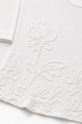 Close-up of a white short-sleeve top with tonal floral embroidery and textured applique along the hem.